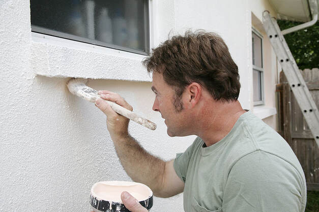 A painter in Norwalk, Connecticut, cuts edges around windows with a brush.