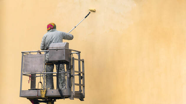 Man on a lifting platform painting the building wall with a roller exterior outdoors in Norwalk, CT.