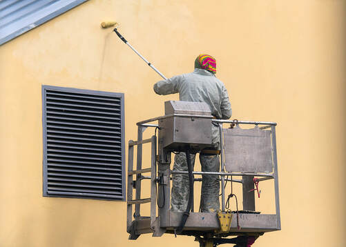 Painter working on a commercial space wall in Norwalk, CT, using a roller to apply white paint.