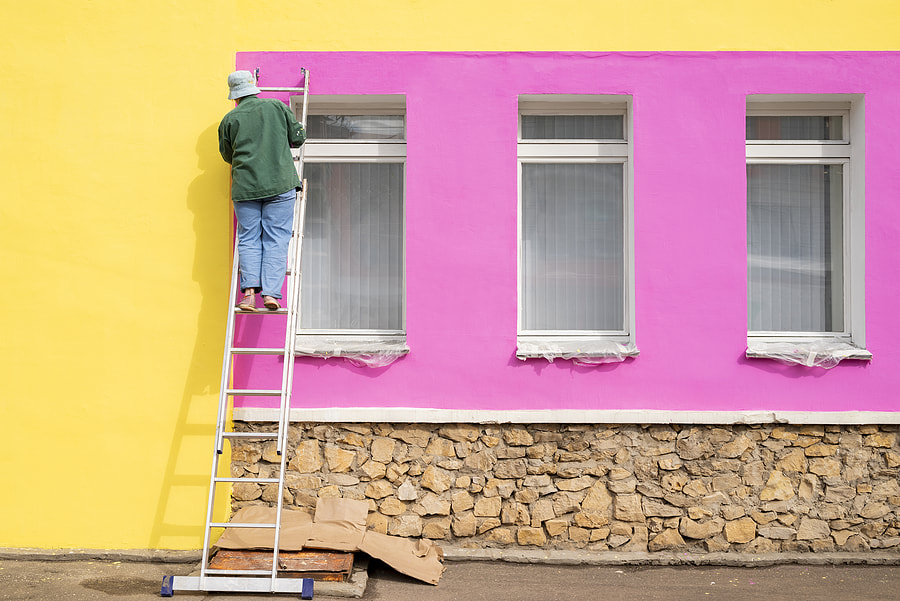 A female painter paints the wall of the facade of a building while standing on the stairs in Norwalk, CT.